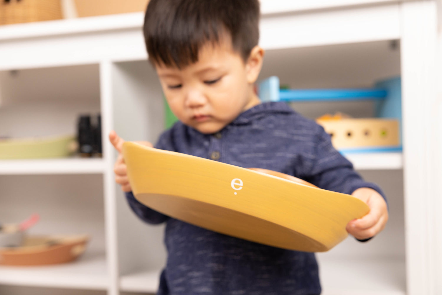 toddler holding Montessori spun bamboo tray and curiously looking inside