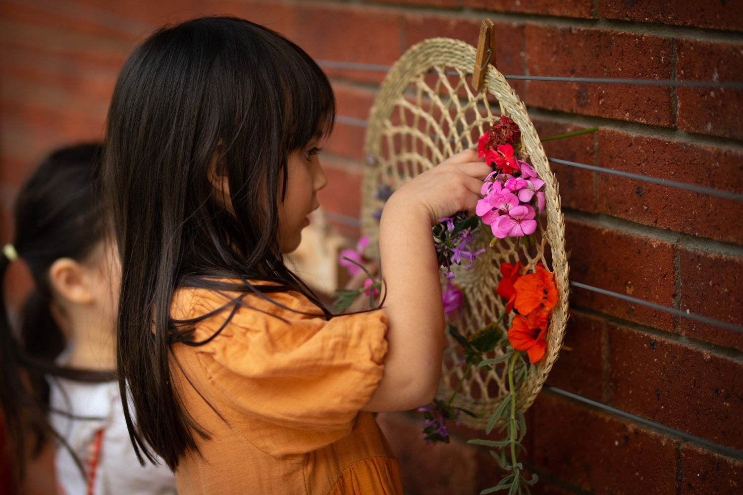 Children focussing as she weaves flowers into a natural seagrass loom