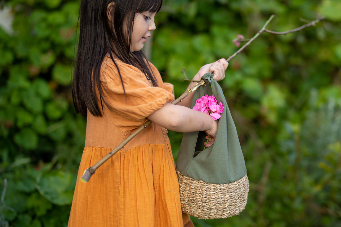 Child placing fresh picked flowers into outdoor Montessori basket tied to a stick