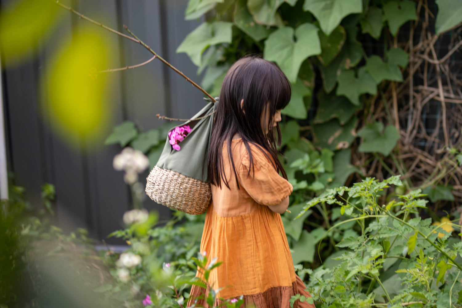 Child roaming the garden with her outdoor Montessori inspired basket tied to a stick