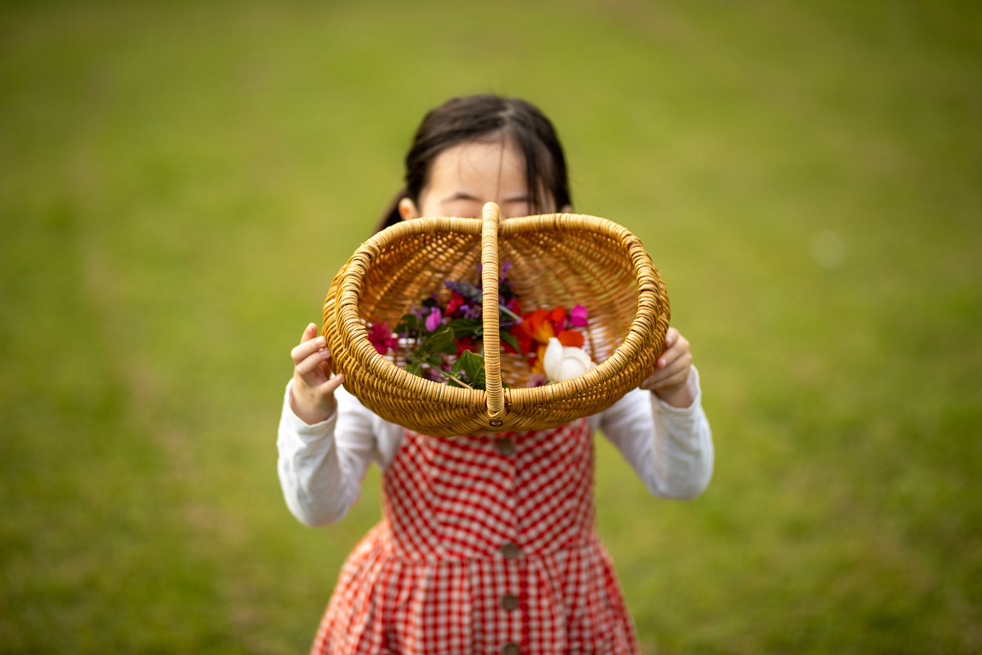 Child holding up child sized garden basket with assortment of flowers inside