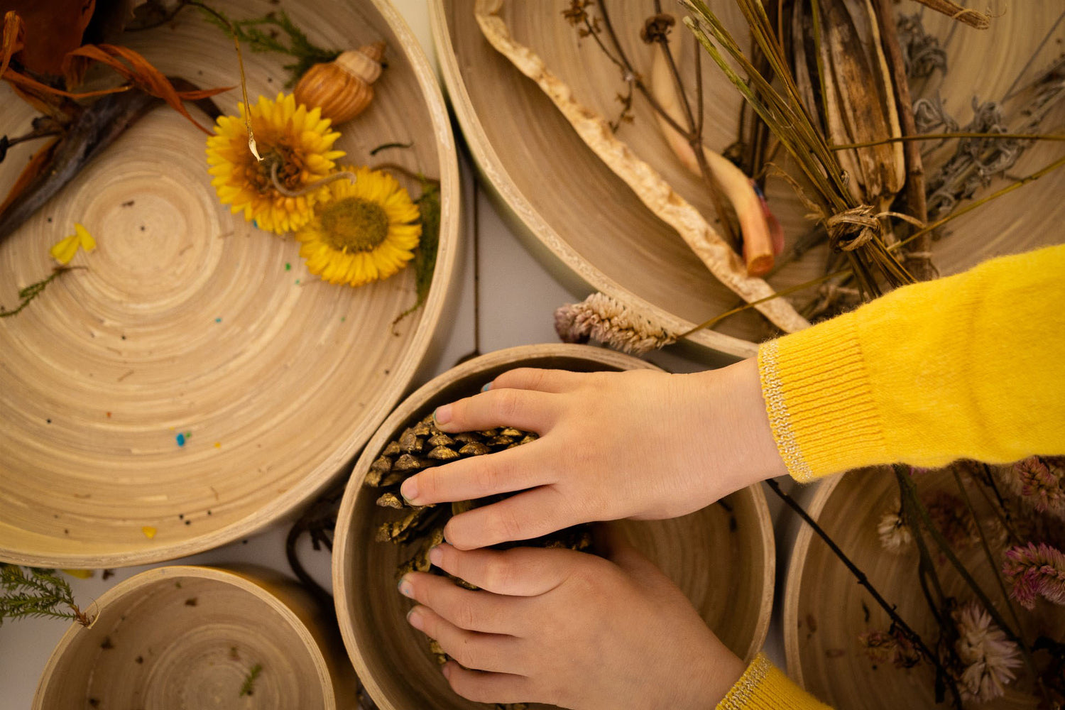 child's hand touching natural materials contained inside Montessori round spun bamboo trays