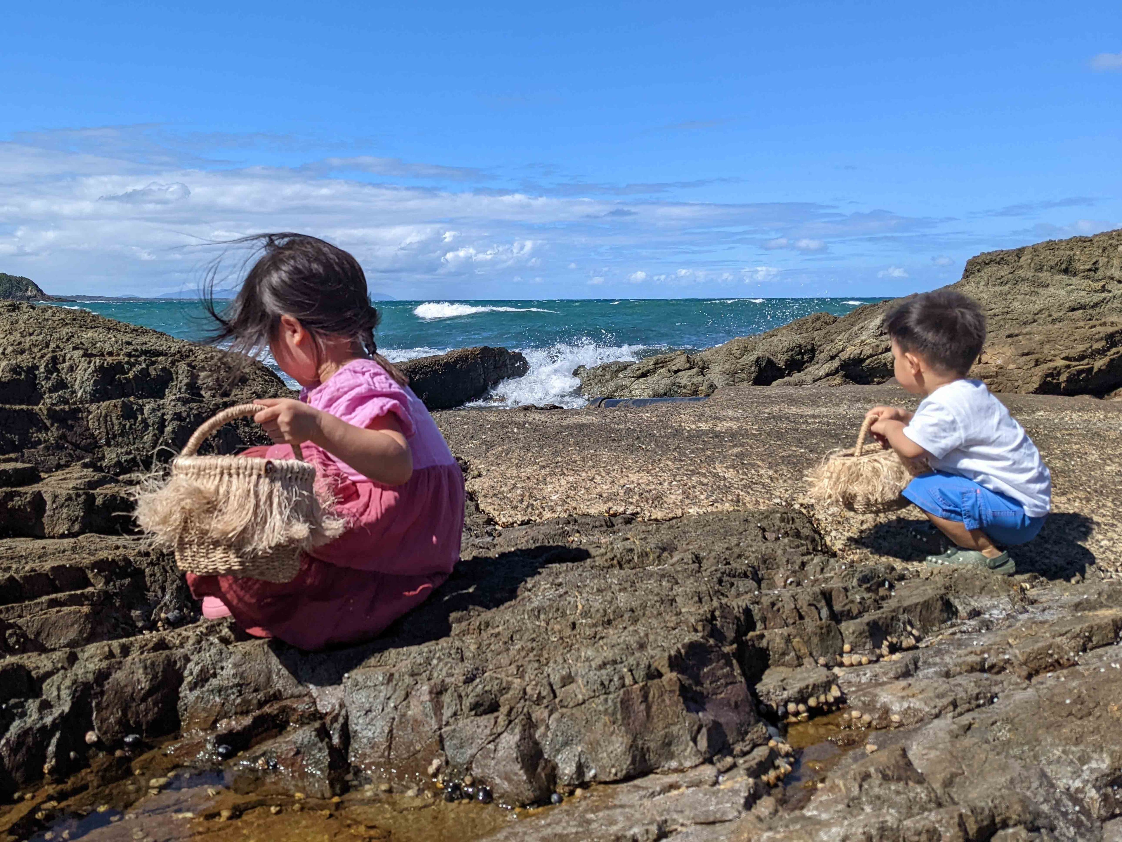 Children collecting natural treasures in rockpools with child sized beach baskets