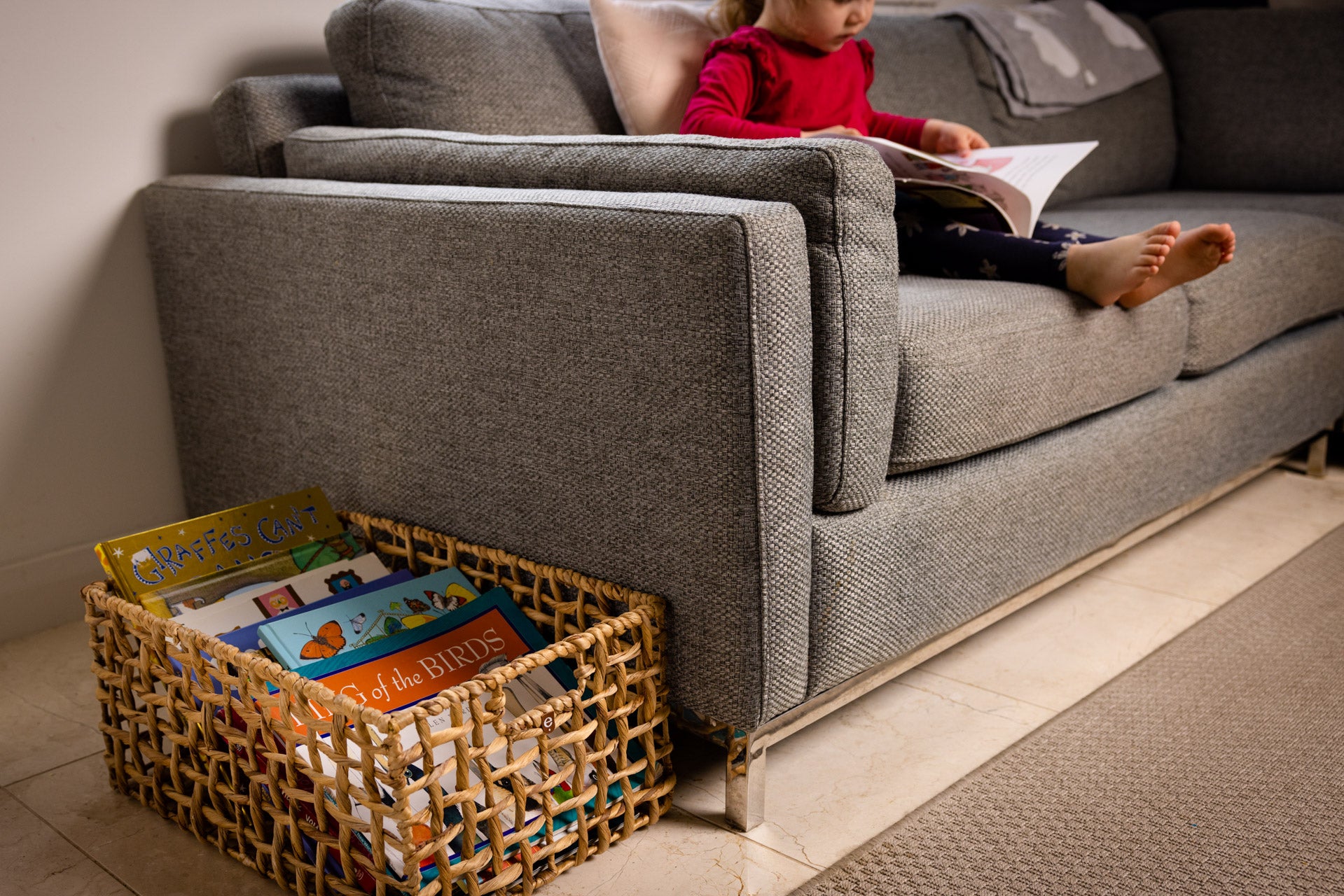 Child reading on a couch beside a Montessori book basket